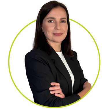 Zespół 1 Kobieta o prostych, ciemnobrązowych włosach i jasnej cerze stoi pewnie ze skrzyżowanymi ramionami. Ma na sobie czarną marynarkę na białym topie i lekko się uśmiecha. Otacza ją jasnozielony okrąg na białym tle.